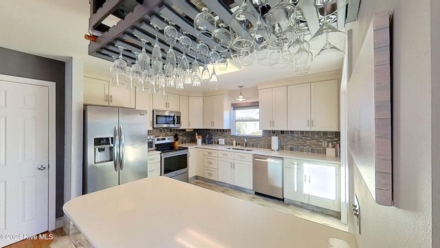 kitchen featuring sink, white cabinetry, backsplash, stainless steel appliances, and decorative light fixtures