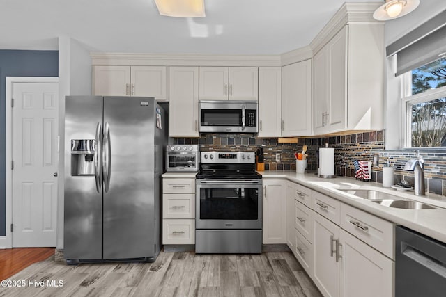 kitchen featuring stainless steel appliances, a sink, tasteful backsplash, light countertops, and white cabinetry