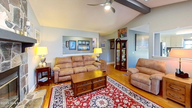 living room featuring a stone fireplace, lofted ceiling with beams, light hardwood / wood-style floors, and ceiling fan