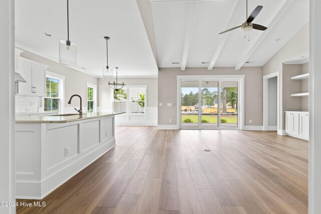 unfurnished living room featuring a wealth of natural light, sink, ceiling fan with notable chandelier, and light wood-type flooring