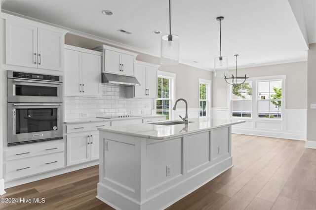 kitchen with double oven, white cabinetry, sink, and a center island with sink