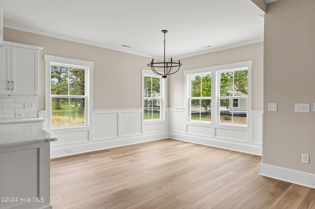 unfurnished dining area with a healthy amount of sunlight, light hardwood / wood-style floors, crown molding, and an inviting chandelier