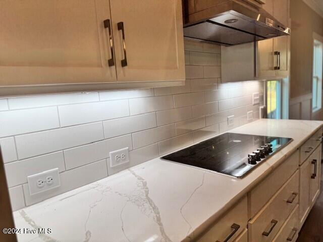 kitchen with light brown cabinets, light stone counters, decorative backsplash, black electric stovetop, and exhaust hood