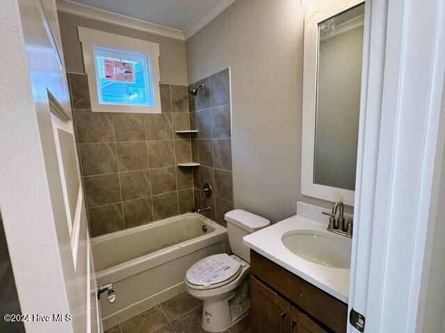 full bathroom with tile patterned flooring, crown molding, toilet, vanity, and tiled shower / bath