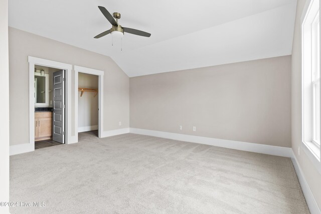 unfurnished bedroom with ensuite bath, ceiling fan, vaulted ceiling, a walk in closet, and carpet