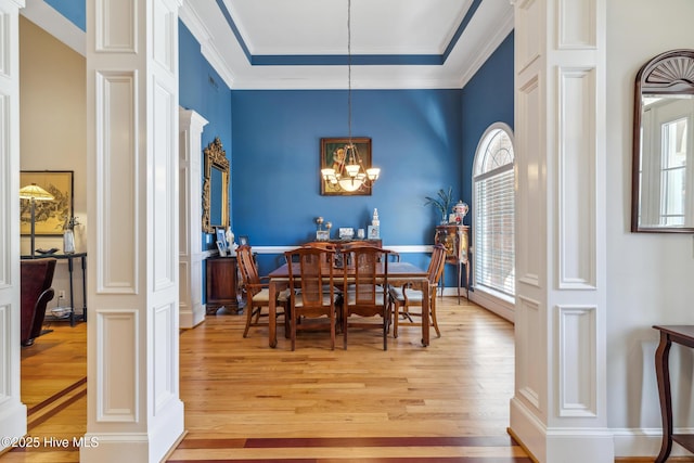 dining area with light wood-type flooring, ornate columns, crown molding, and a notable chandelier