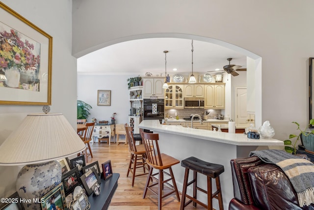 kitchen with decorative light fixtures, black oven, cream cabinets, light wood-type flooring, and ceiling fan