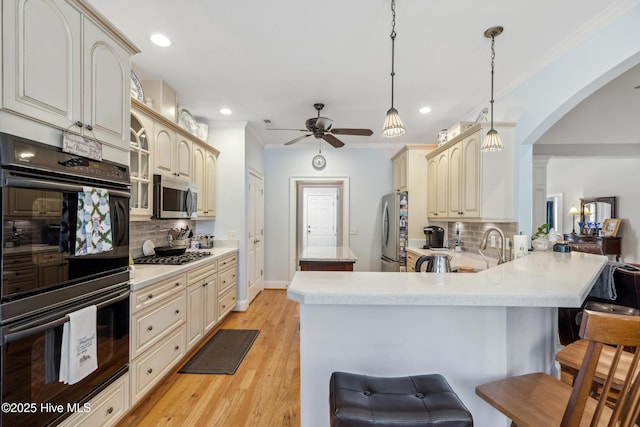 kitchen featuring a kitchen bar, kitchen peninsula, stainless steel appliances, decorative light fixtures, and cream cabinets