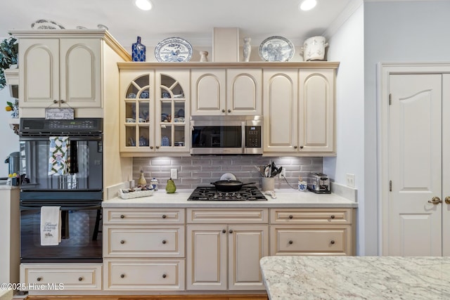 kitchen with light stone counters, backsplash, appliances with stainless steel finishes, and cream cabinetry