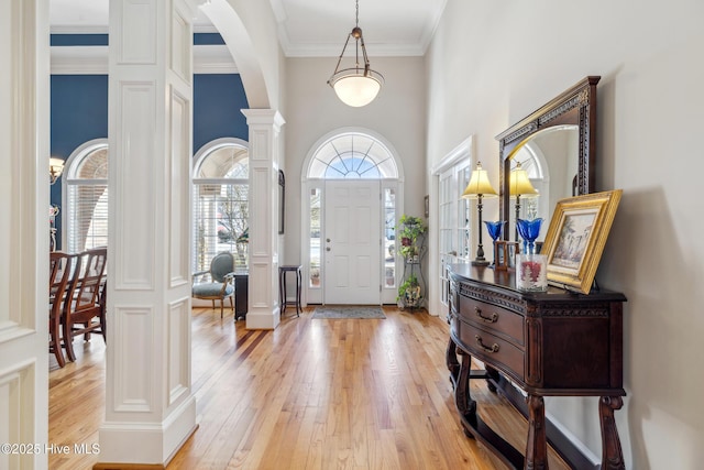 entrance foyer featuring light wood-type flooring, a towering ceiling, crown molding, and ornate columns