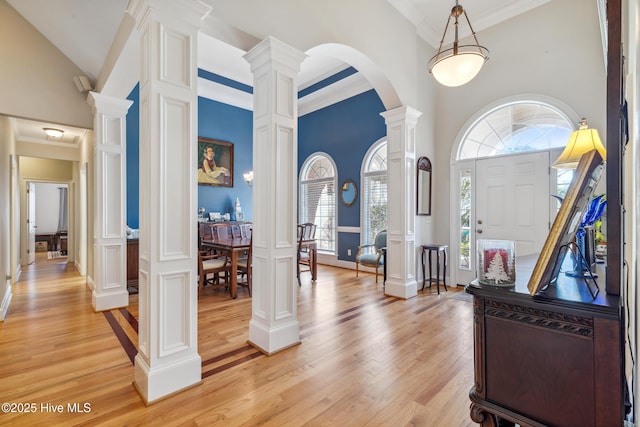 entryway featuring crown molding, light wood-type flooring, a high ceiling, and ornate columns