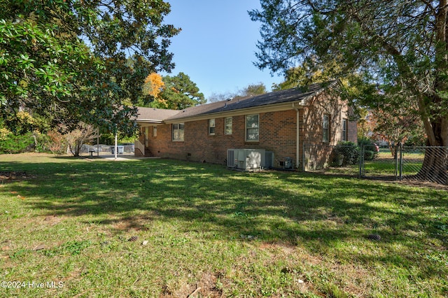 rear view of property featuring central air condition unit and a lawn