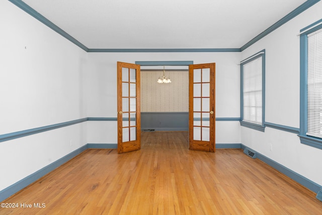 empty room featuring wood-type flooring, crown molding, an inviting chandelier, and french doors