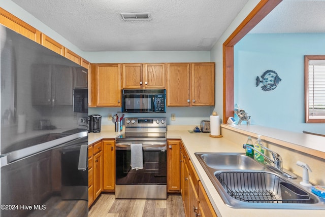 kitchen with black appliances, a textured ceiling, sink, and light hardwood / wood-style flooring