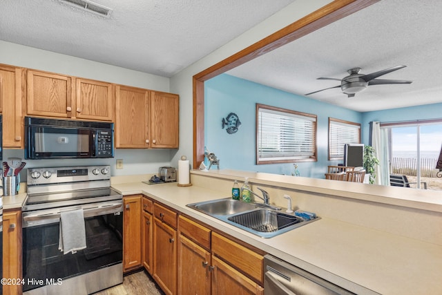 kitchen featuring stainless steel appliances, a textured ceiling, sink, ceiling fan, and light hardwood / wood-style flooring