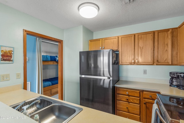 kitchen with sink, a textured ceiling, and stainless steel fridge