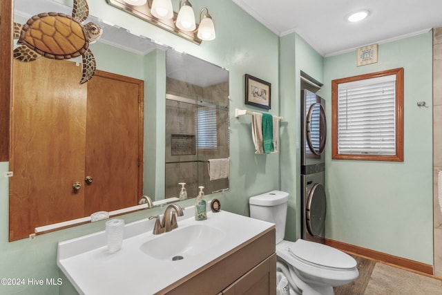 bathroom featuring ornamental molding, vanity, stacked washer / dryer, a shower with shower door, and toilet