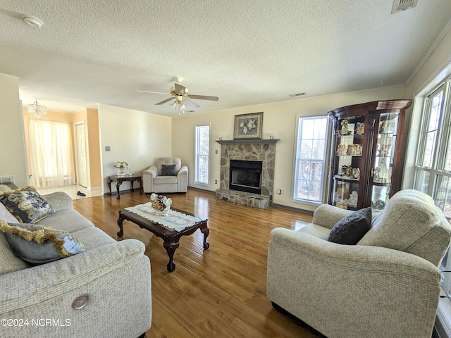 living room featuring a stone fireplace, a wealth of natural light, a textured ceiling, and hardwood / wood-style flooring