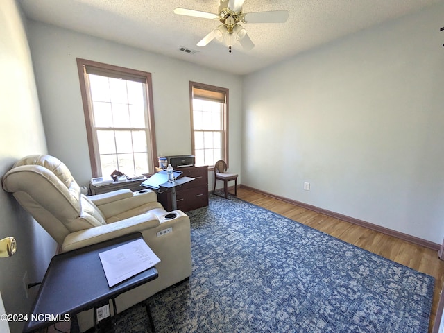 living area with a textured ceiling, hardwood / wood-style flooring, and ceiling fan