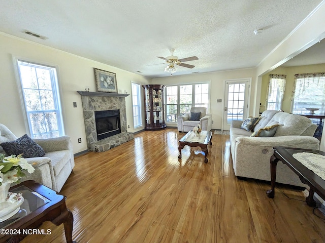 117 Longwood Dr, Stella, NC 28582 - living room featuring wood finished floors, a textured ceiling, ornamental molding, a ceiling fan, and a stone fireplace
