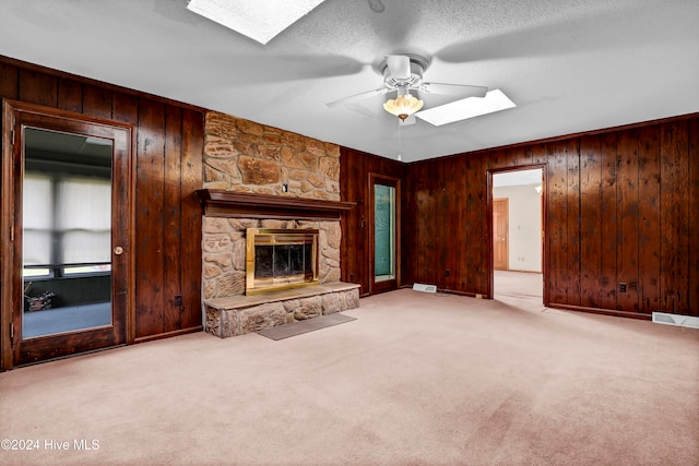 unfurnished living room with wooden walls, a fireplace, ceiling fan, and light colored carpet