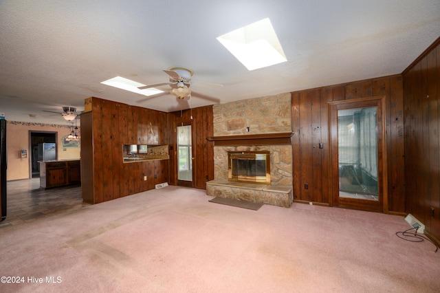 unfurnished living room with ceiling fan, carpet floors, wooden walls, and a skylight