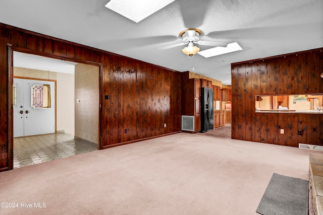 unfurnished living room with wooden walls, a skylight, ceiling fan, and light colored carpet