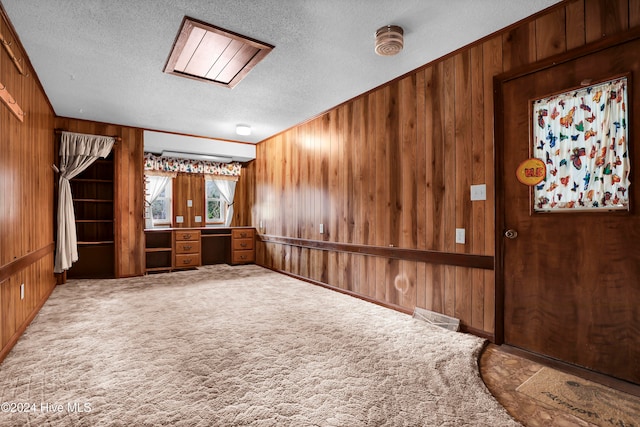 carpeted spare room with a textured ceiling and wood walls