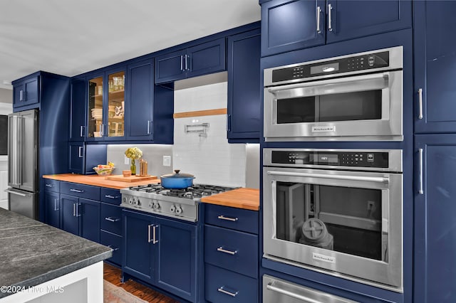 kitchen featuring backsplash, blue cabinets, dark hardwood / wood-style flooring, butcher block counters, and stainless steel appliances