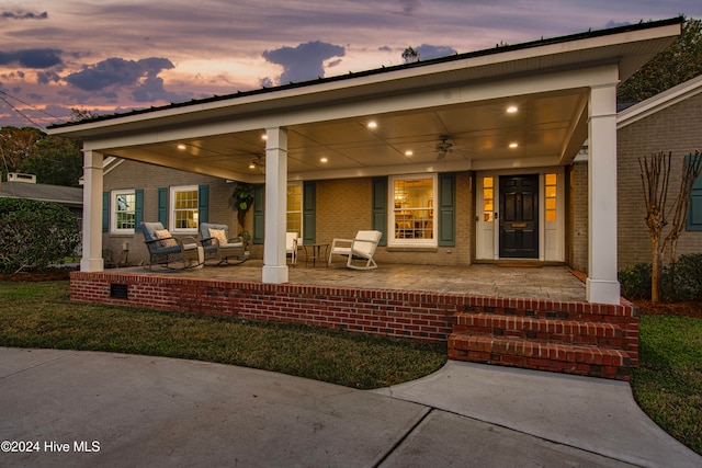 back house at dusk with ceiling fan and covered porch