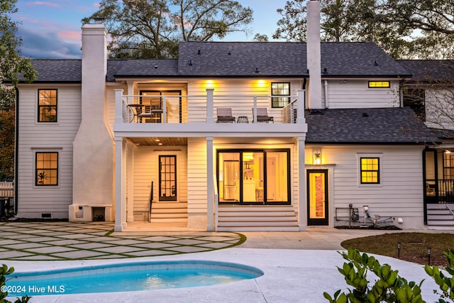 back house at dusk with a balcony and a patio area