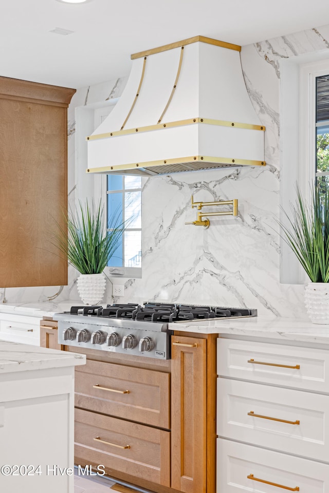 kitchen featuring tasteful backsplash, light stone counters, custom range hood, stainless steel gas cooktop, and white cabinets