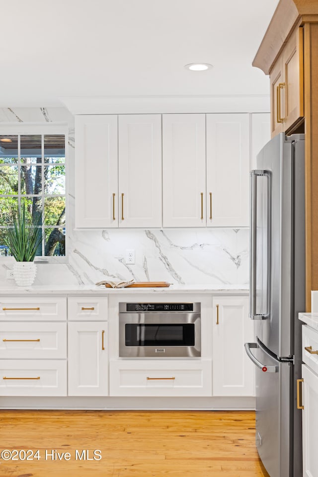 kitchen with appliances with stainless steel finishes, backsplash, light stone counters, light hardwood / wood-style floors, and white cabinetry