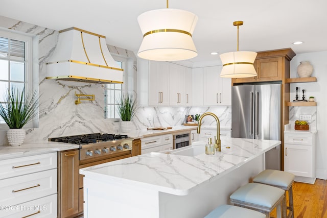 kitchen featuring appliances with stainless steel finishes, premium range hood, pendant lighting, and an island with sink