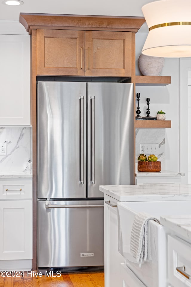 kitchen with backsplash, white cabinets, light stone countertops, light hardwood / wood-style floors, and high end fridge