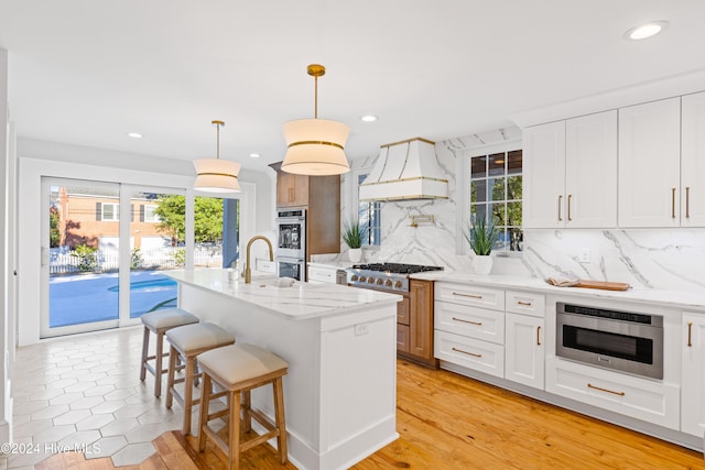 kitchen featuring light stone countertops, a kitchen island with sink, decorative light fixtures, white cabinets, and light hardwood / wood-style floors