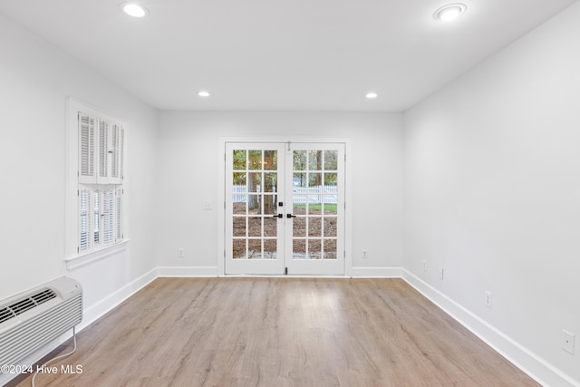 empty room with a wall mounted air conditioner, french doors, and light hardwood / wood-style floors