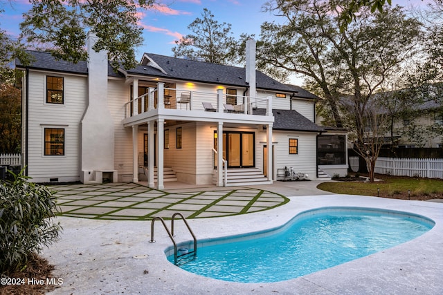 back house at dusk with a fenced in pool, a patio area, and a balcony