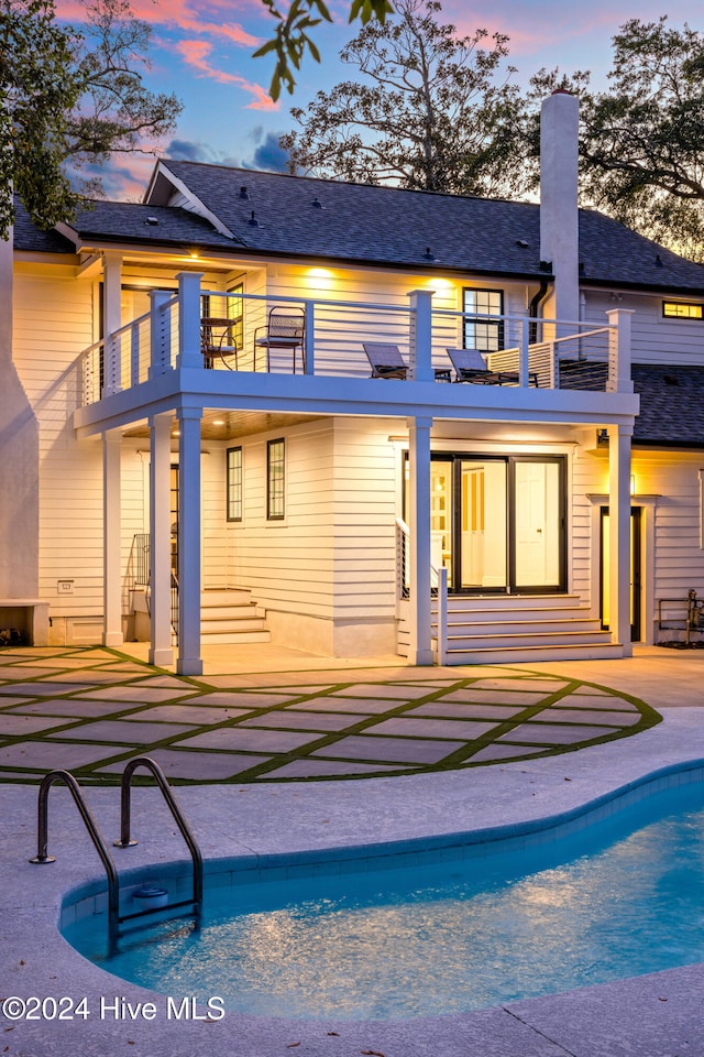 back house at dusk featuring a patio and a balcony