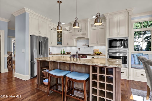 kitchen featuring appliances with stainless steel finishes, backsplash, ornamental molding, pendant lighting, and an island with sink