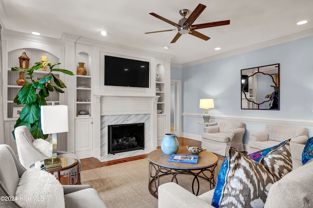 living room featuring ornamental molding, ceiling fan, built in features, a premium fireplace, and hardwood / wood-style floors