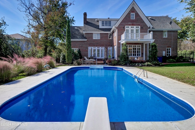 view of swimming pool featuring a lawn, a diving board, and french doors