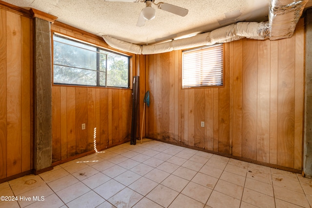 spare room featuring ceiling fan, a healthy amount of sunlight, a textured ceiling, and wooden walls