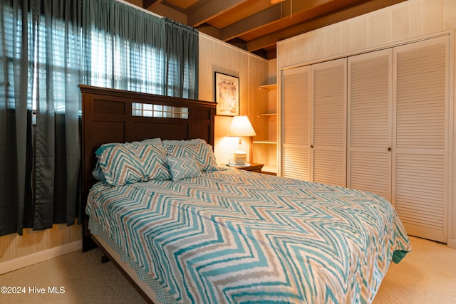 carpeted bedroom with beam ceiling and a closet