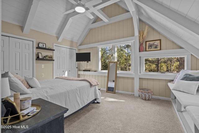 carpeted bedroom featuring ceiling fan, beam ceiling, high vaulted ceiling, and multiple closets