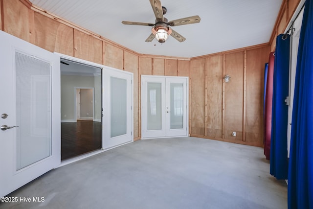 unfurnished room featuring ceiling fan, french doors, an AC wall unit, concrete floors, and wooden walls