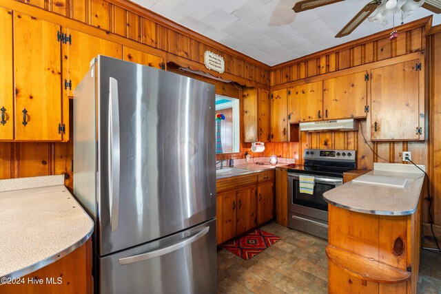 kitchen with appliances with stainless steel finishes, ceiling fan, wooden walls, and sink