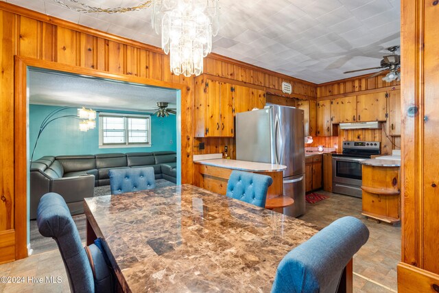 kitchen featuring ornamental molding, ceiling fan with notable chandelier, stainless steel appliances, and wooden walls