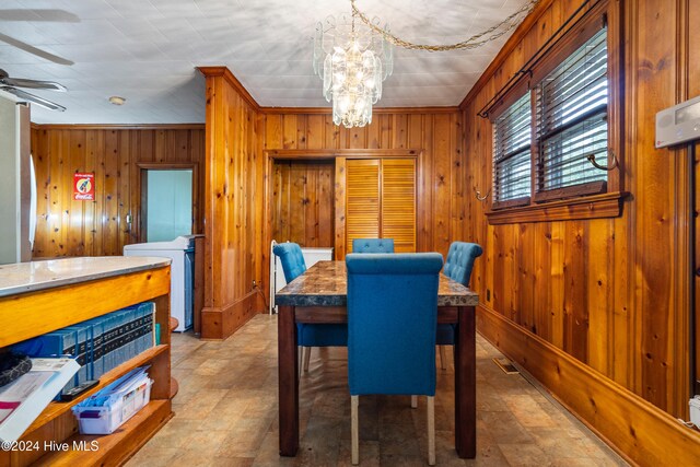 dining area with wood walls, ceiling fan with notable chandelier, and ornamental molding