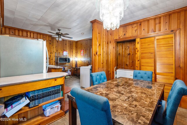 dining space featuring wooden walls, light colored carpet, ceiling fan with notable chandelier, and ornamental molding